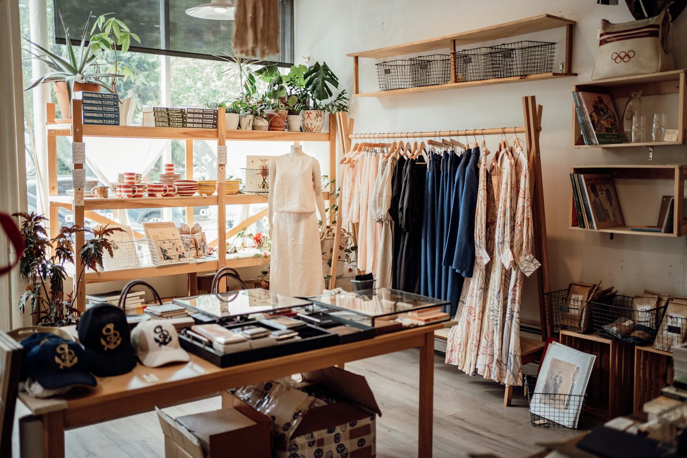 A bright modern boutique, rails of clothing and a display table.